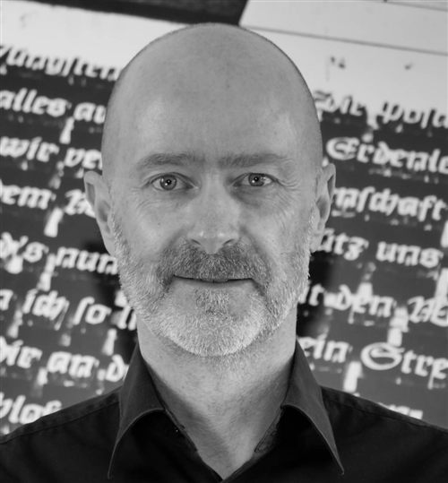 Porträt von Michael Brey vor einer Wand mit Frakturschrift-Zitaten